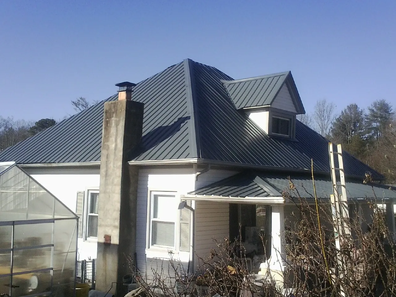 Dark blue standing seam metal roof on a white farmhouse with dormer — Slate & Tile Roof Repair by Roofing Brothers in New Caney