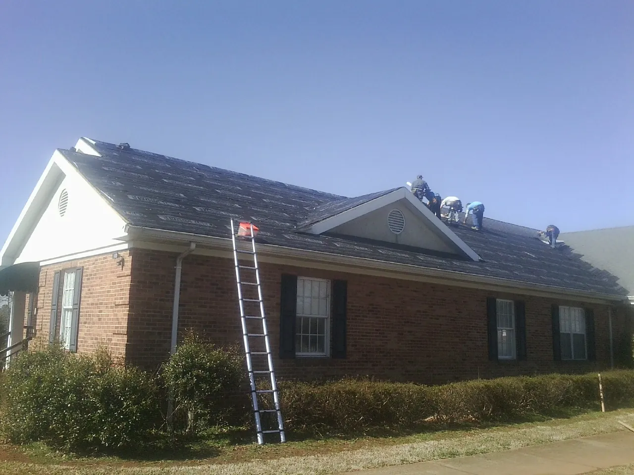 Crew tearing shingles off a brick ranch roof with a ladder set — Emergency Roof Repair work by our crew in New Caney