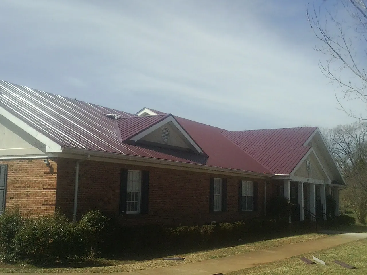 Red metal roof with gabled entries on a long brick building, from a Hail Damage Roof Repair job in New Caney
