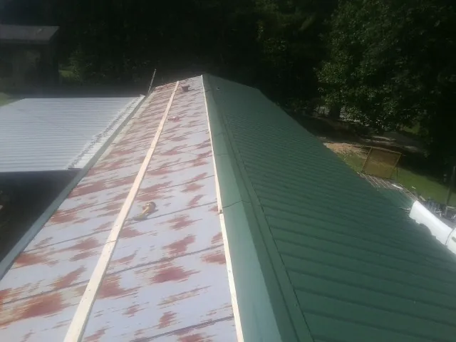 Old rusted panels beside newly installed green metal roofing — Wind Damage Roof Repair by Roofing Brothers in New Caney