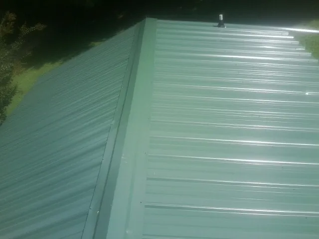 New green metal panels meeting at the ridge of a roof — Flat Roof Repair work by our crew in New Caney