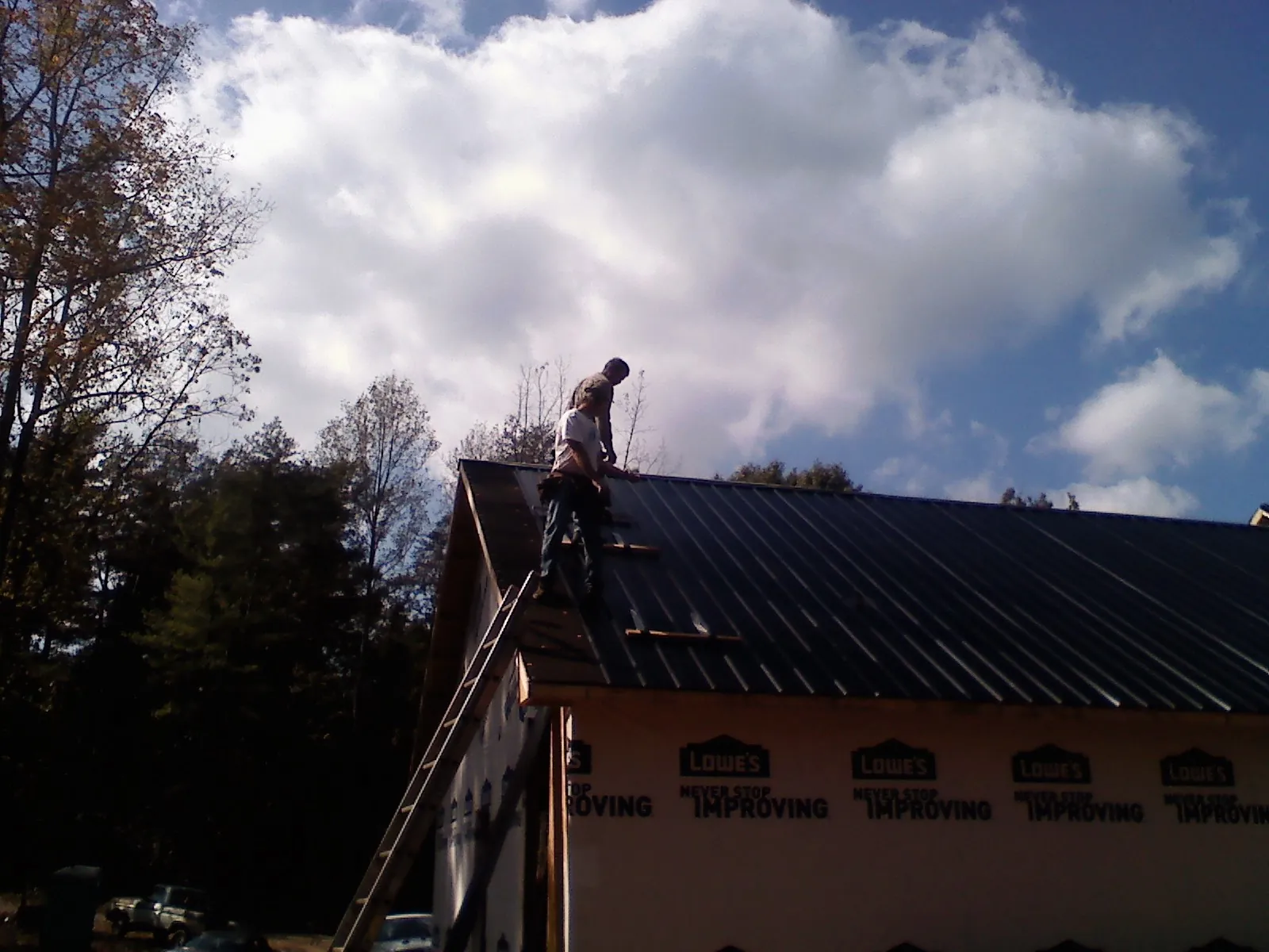 Roofer fastening dark metal panels high against a cloudy sky, from a Roof Inspection job in New Caney