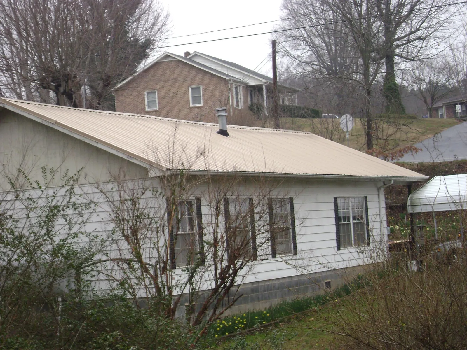 Tan metal roof on a white sided house set into a hillside — Commercial Roofing by Roofing Brothers in New Caney